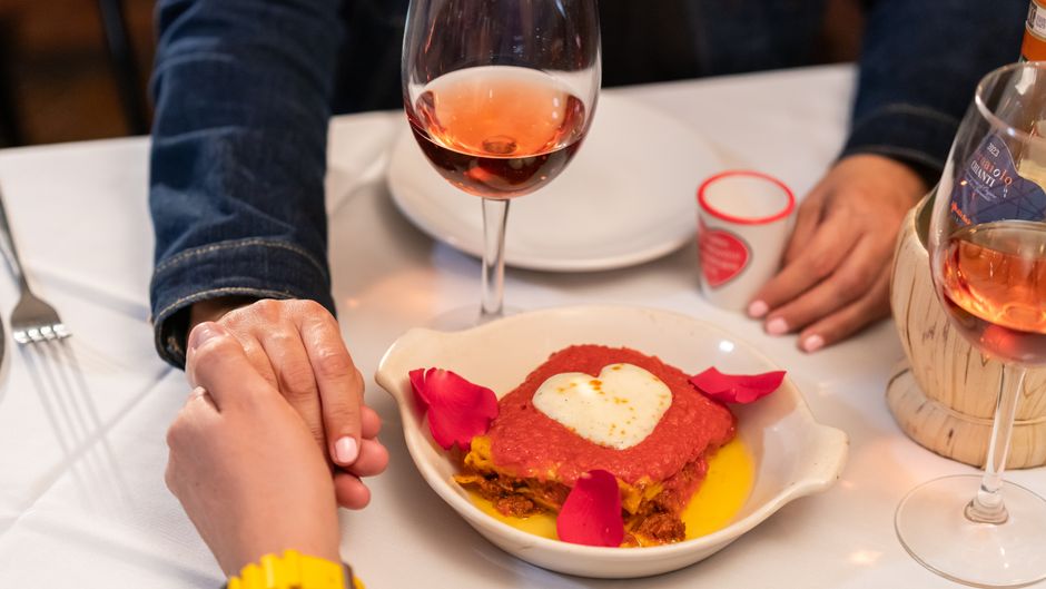 A romantic dinner scene with a heart-shaped dish, rose wine, and couple holding hands
