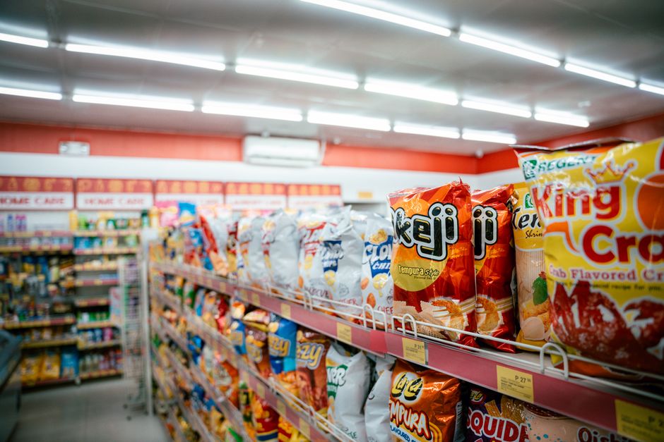 Rækker af emballerede snackposer på en oplyst hylde i et supermarked