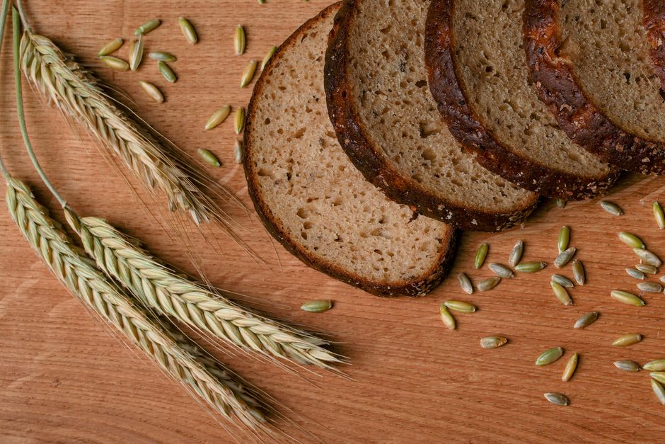A rustic arrangement of sliced wheat bread with wheat ears and grains on a wooden surface