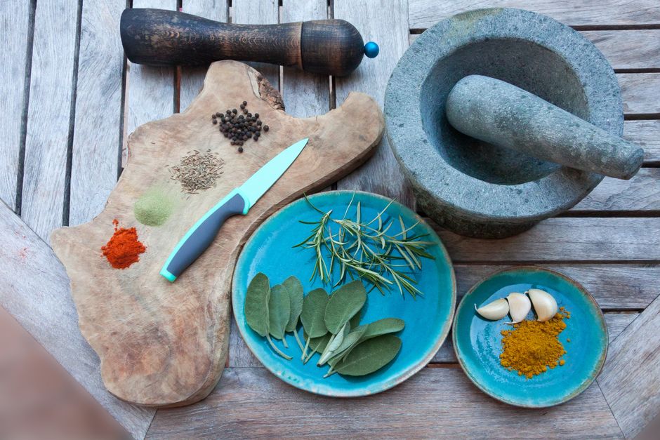 Fresh herbs, garlic, and ground spices laid out on plates and a cutting board