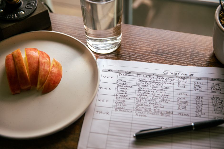 Sliced apple, a glass of water, and a handwritten calorie tracking sheet on a table