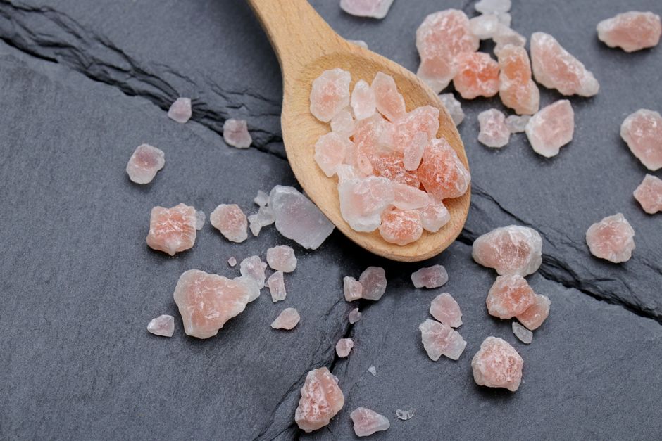 Close-up of Himalayan pink salt crystals on a wooden spoon and slate background, perfect for culinary use