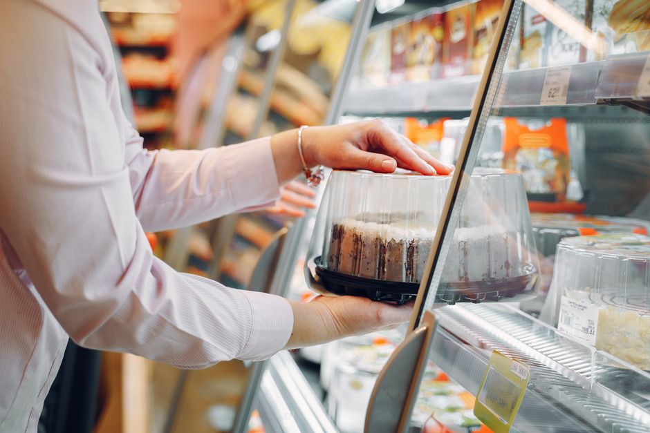 A woman choosing a packaged cake from a supermarket chiller