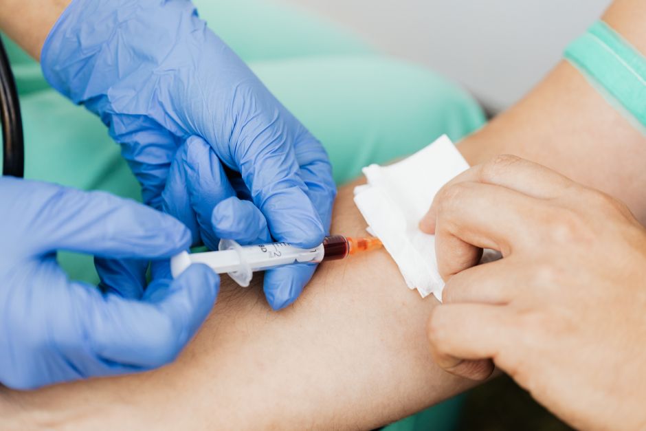 En hånd i handske tager en blodprøve fra en patients arm