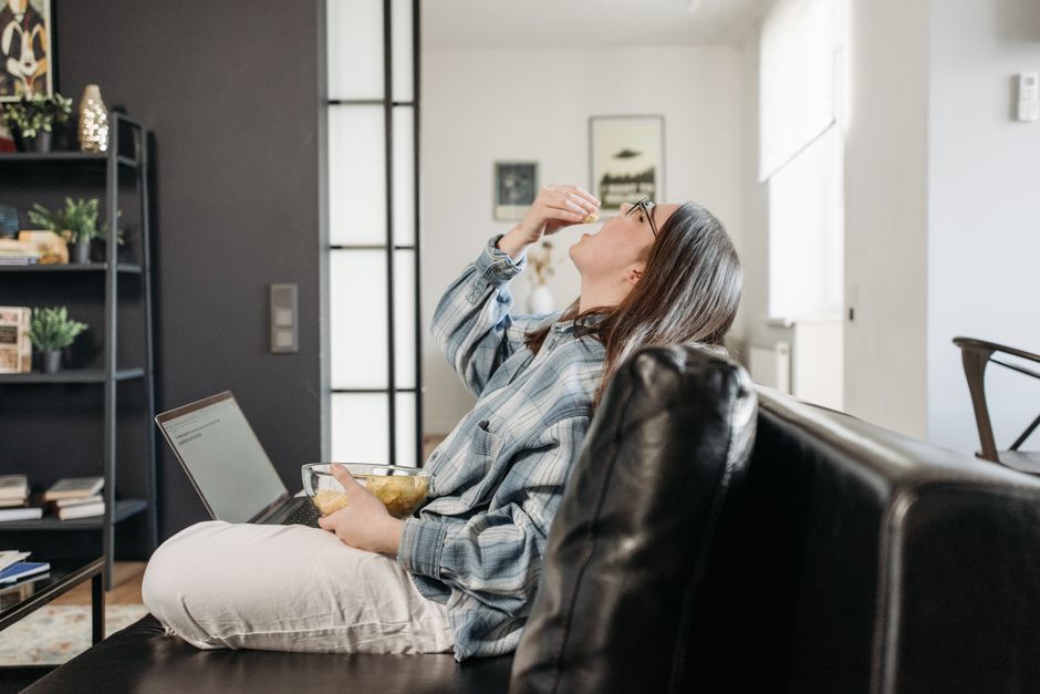 Woman at a desk with a laptop eating a bowl of chips