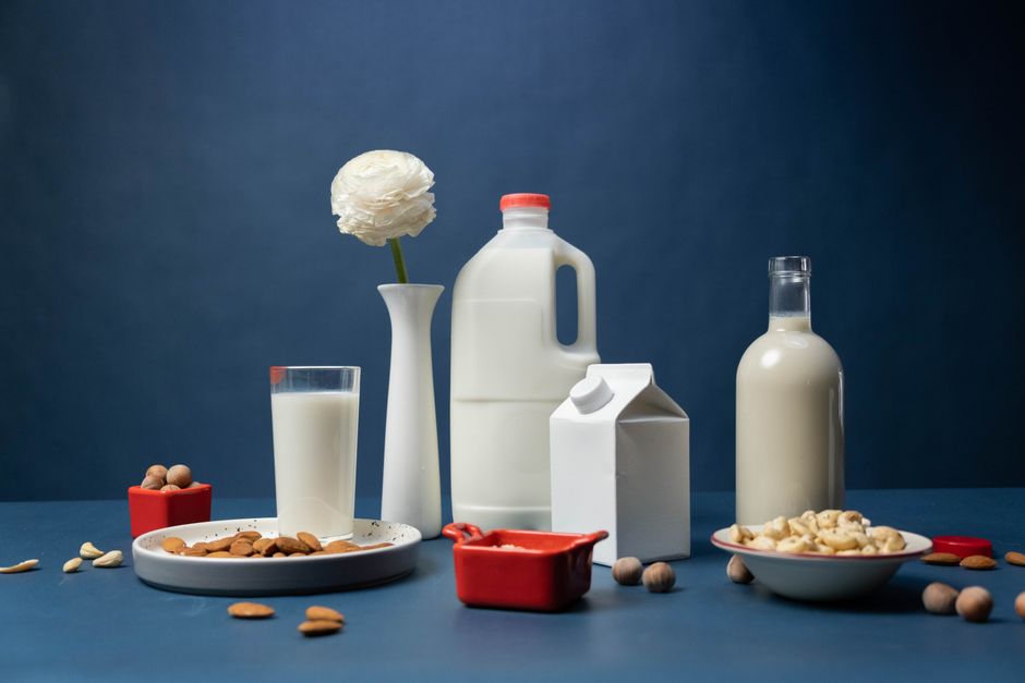 Flasker og et glas med forskellige plantebaserede mælkedrikke med nødder ved siden af