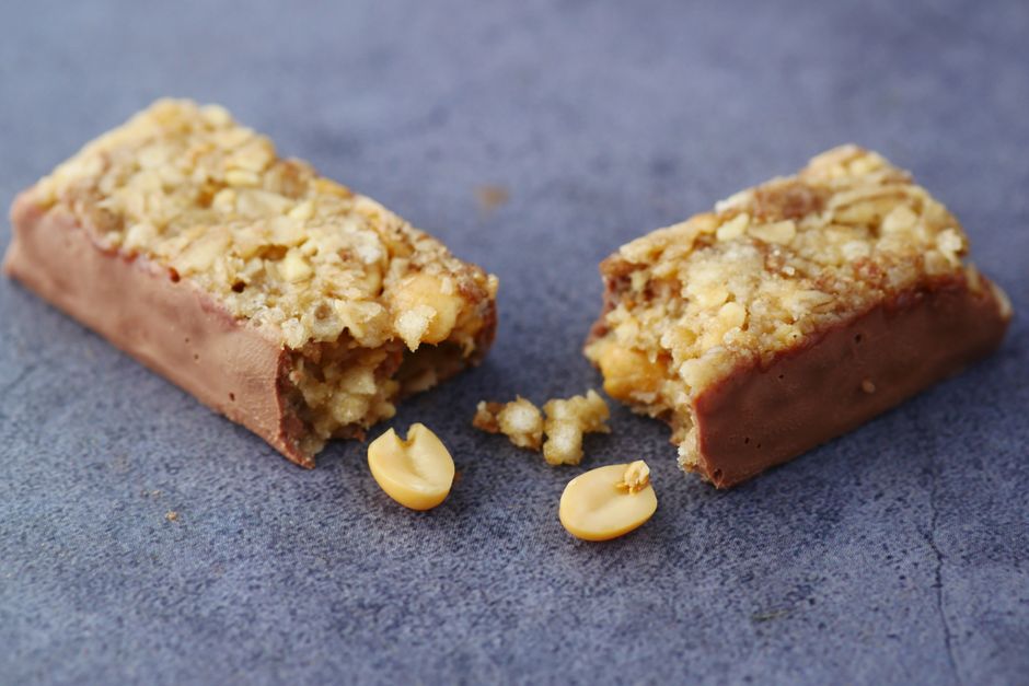 A protein bar broken in half next to loose peanuts