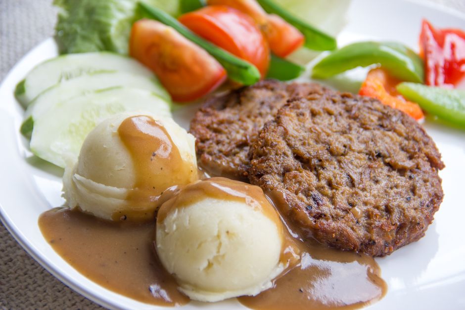 A plant-based patty served on a plate with vegetables and mashed potato