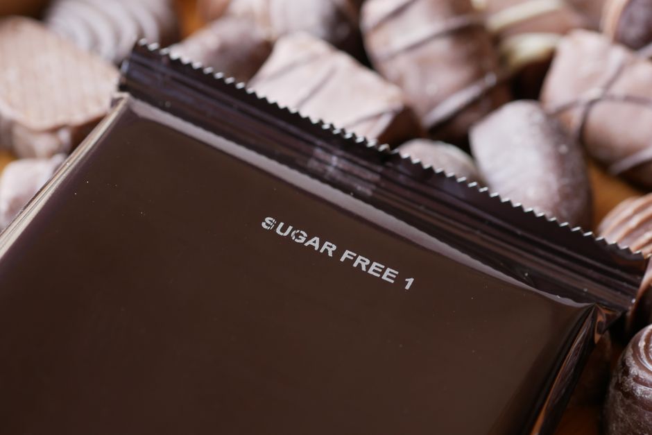 A close-up of a sugar-free chocolate wrapper labeled 'Sugar Free' next to chocolate candies