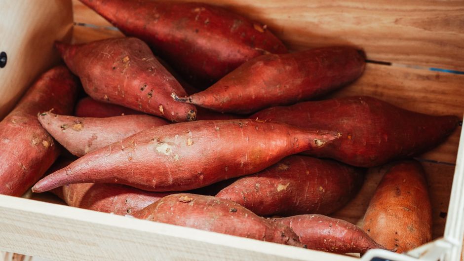 A wooden crate filled with fresh sweet potatoes