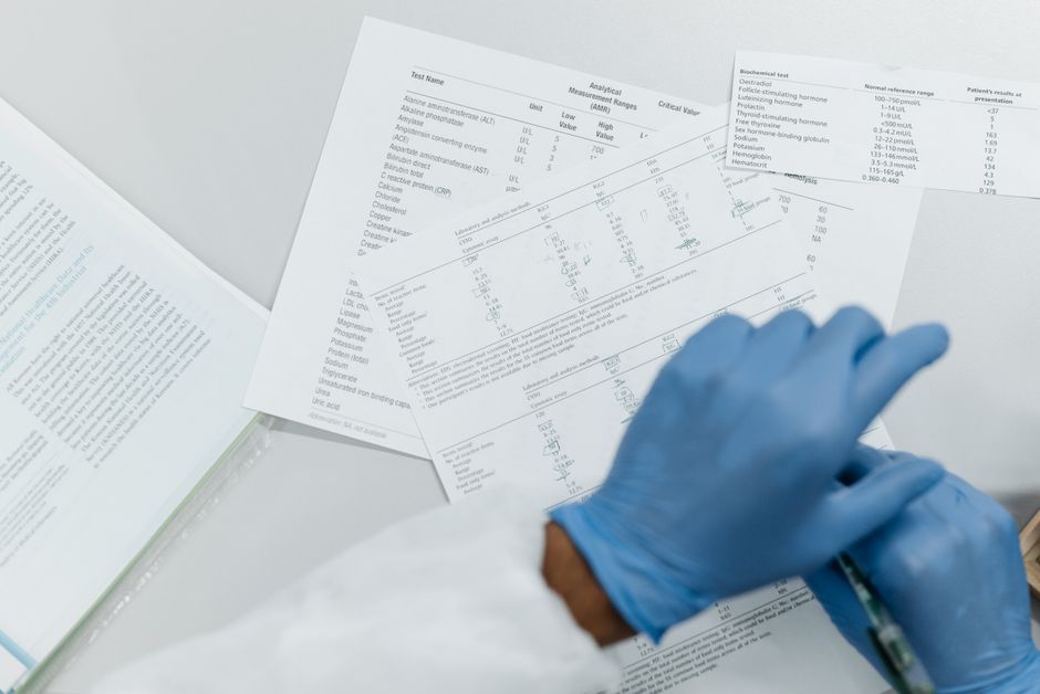 Hænder i handsker gennemgår en udskrevet laboratorierapport med kolesteroltal
