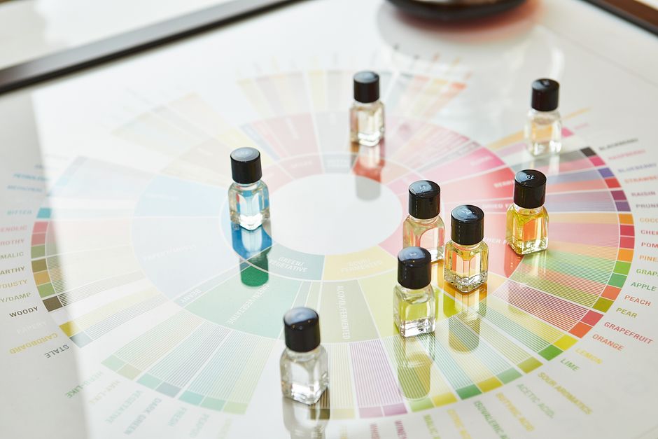 Små glasrør med aromastoffer arrangeret på et farverigt aromahjul
