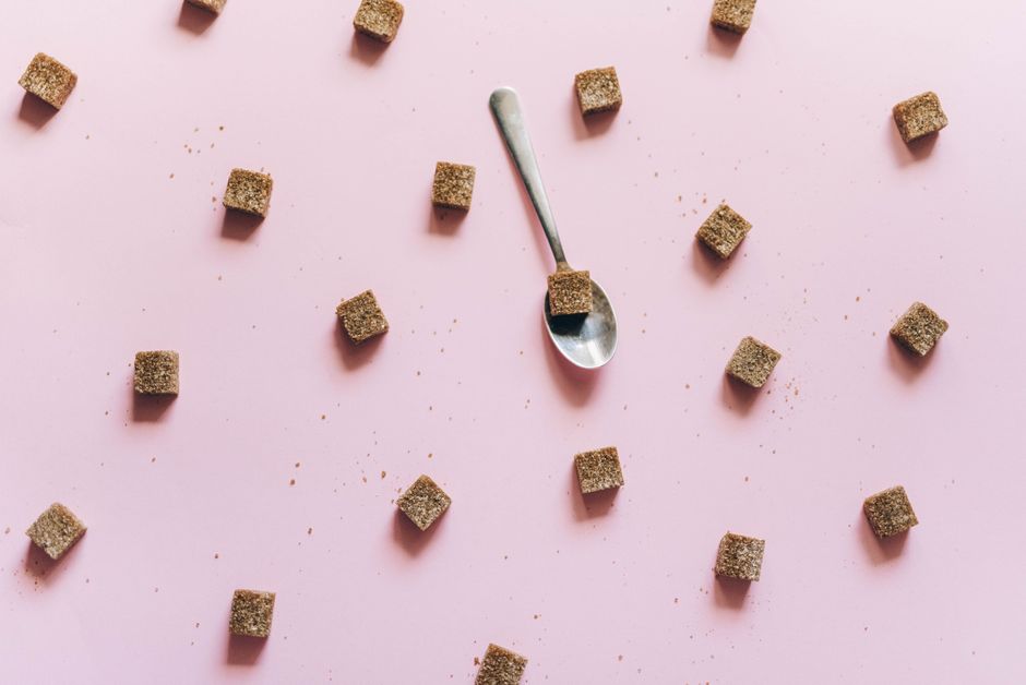 Brown sugar cubes and a spoon scattered across a pink surface