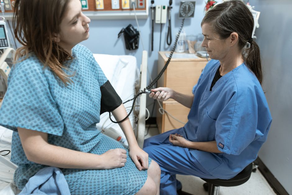 En sygeplejerske måler blodtrykket på en siddende patient i et klinisk lokale